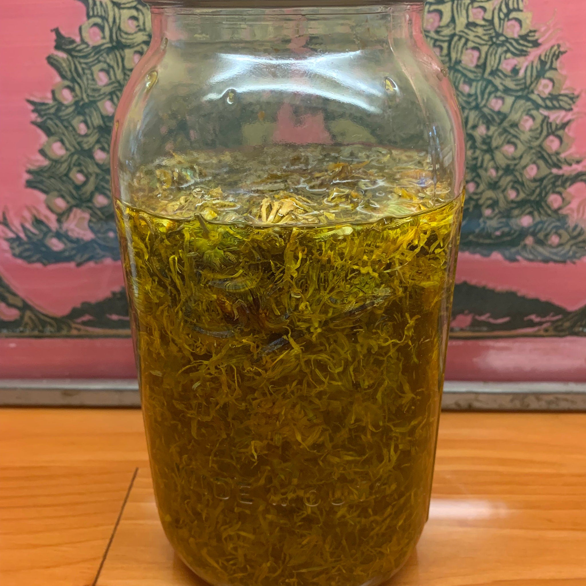 Glass jar with yellow liquid and green plant matter, clear glass, wooden surface