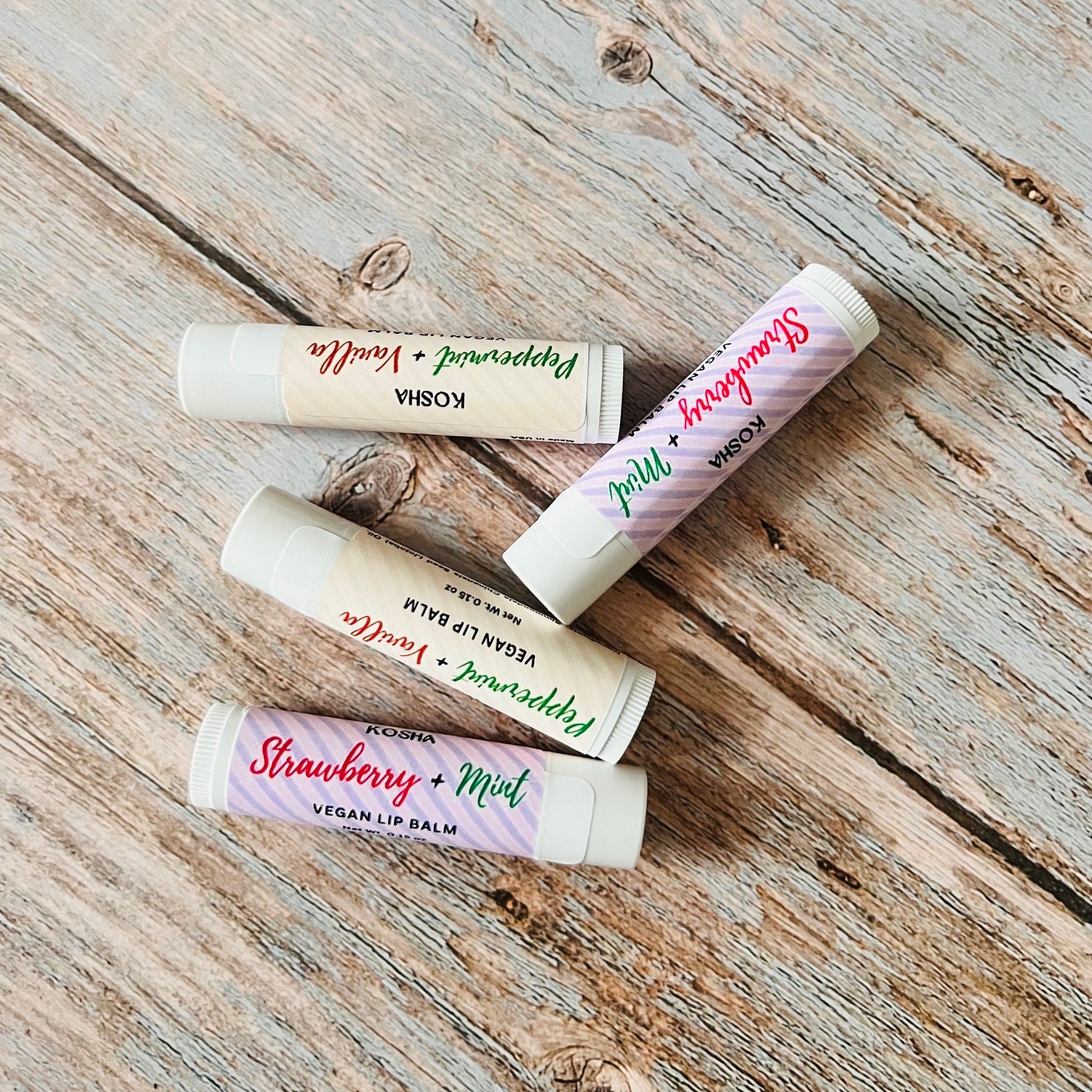 Lip balm tubes with white, striped, and text labels, on wooden surface, KOSHA brand visible