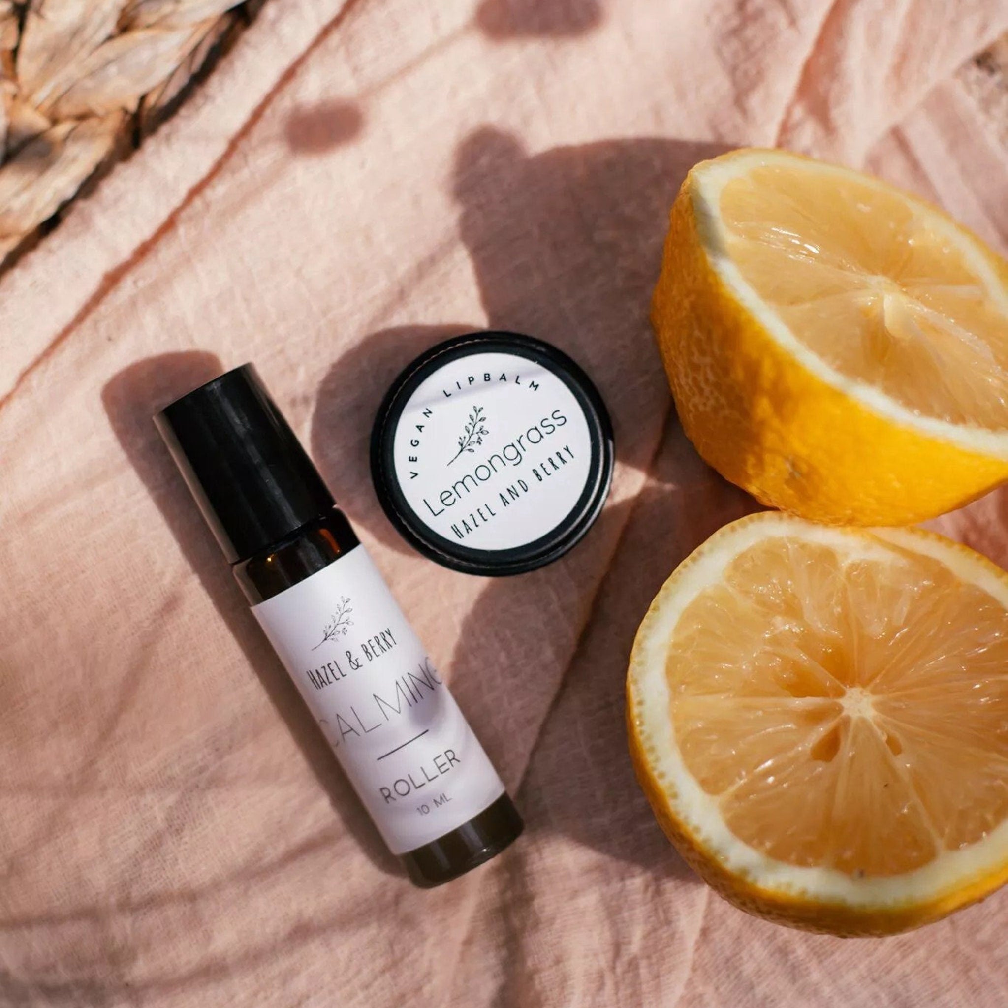 Roller bottle and lip balm with Hazel & Berry branding, on pink fabric with sliced lemon