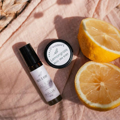 Roller bottle and lip balm with Hazel & Berry branding, on pink fabric with sliced lemon
