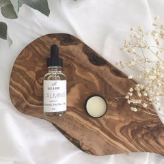 Facial oil bottle with black dropper, white label, and wood grain cutting board