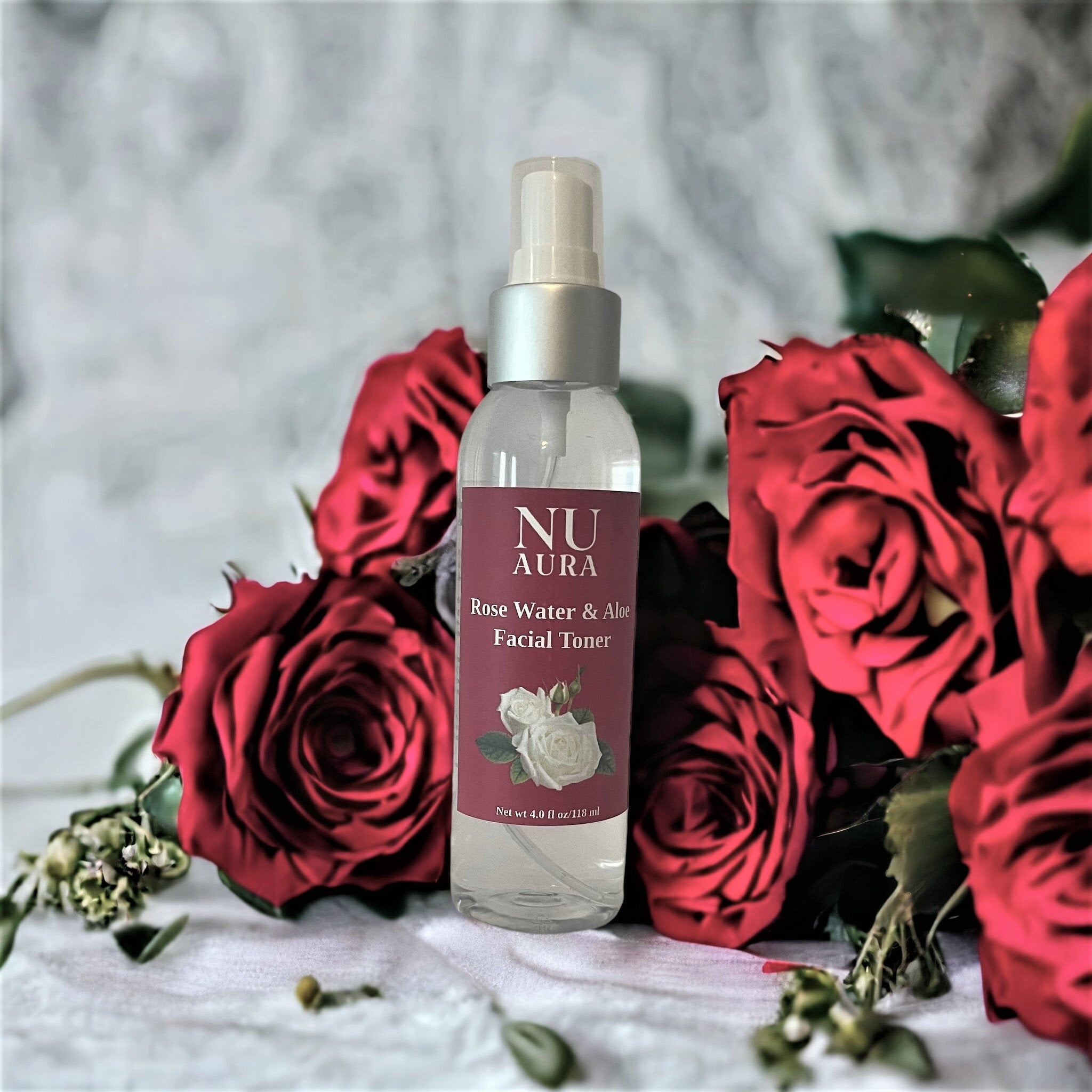 Facial toner bottle with clear glass and silver cap, Nu Aura label, surrounded by red roses