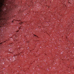 Woman applying shimmering pink mineral eye shadow with fingertip to eyelid, showcasing pigmented color payoff