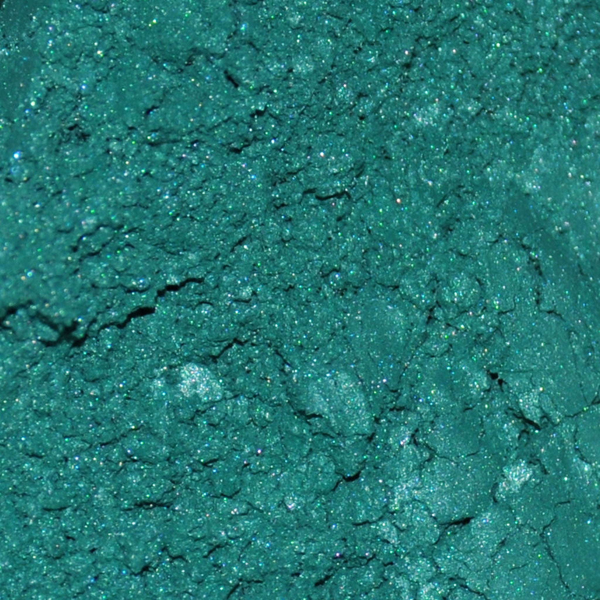 Hand applying pigmented mineral eyeshadow with brush from sifter jar, showing powder texture and color payoff