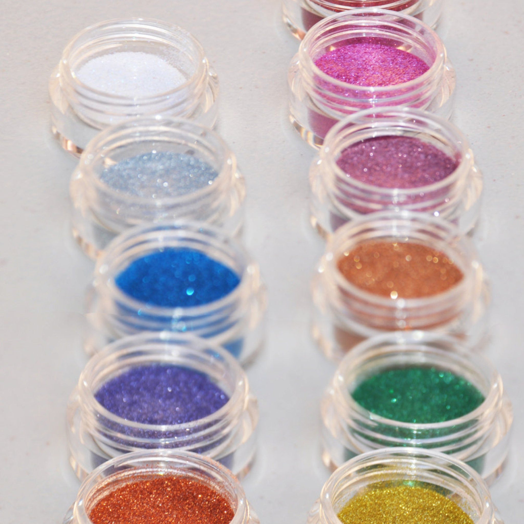 Hand applying shimmering silver glitter eyeshadow from a jar with sifter lid onto eyelid