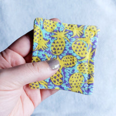 Makeup remover pad with yellow pineapple print fabric held in hand