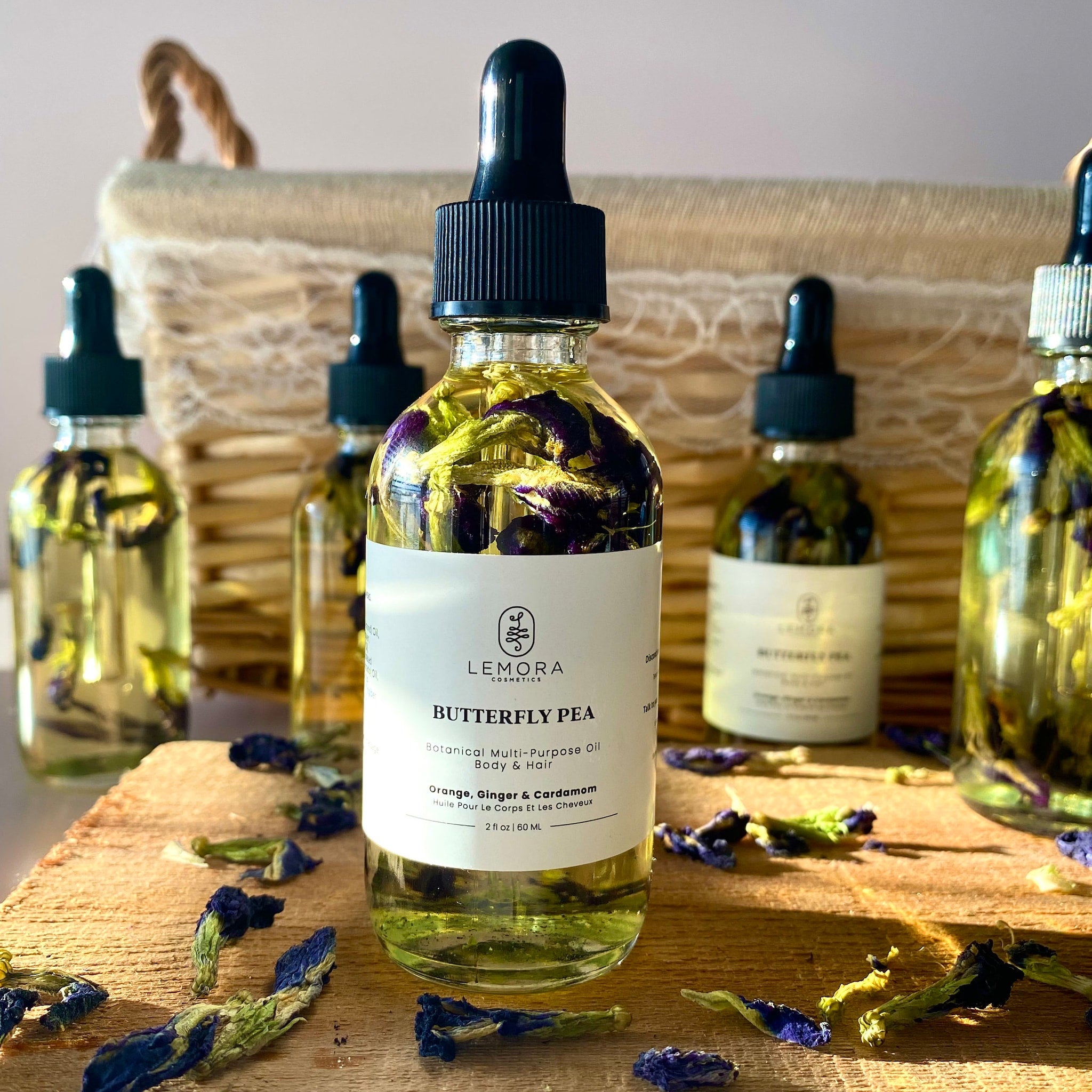 Butterfly pea oil bottles with clear glass, black dropper, and white label on wood surface