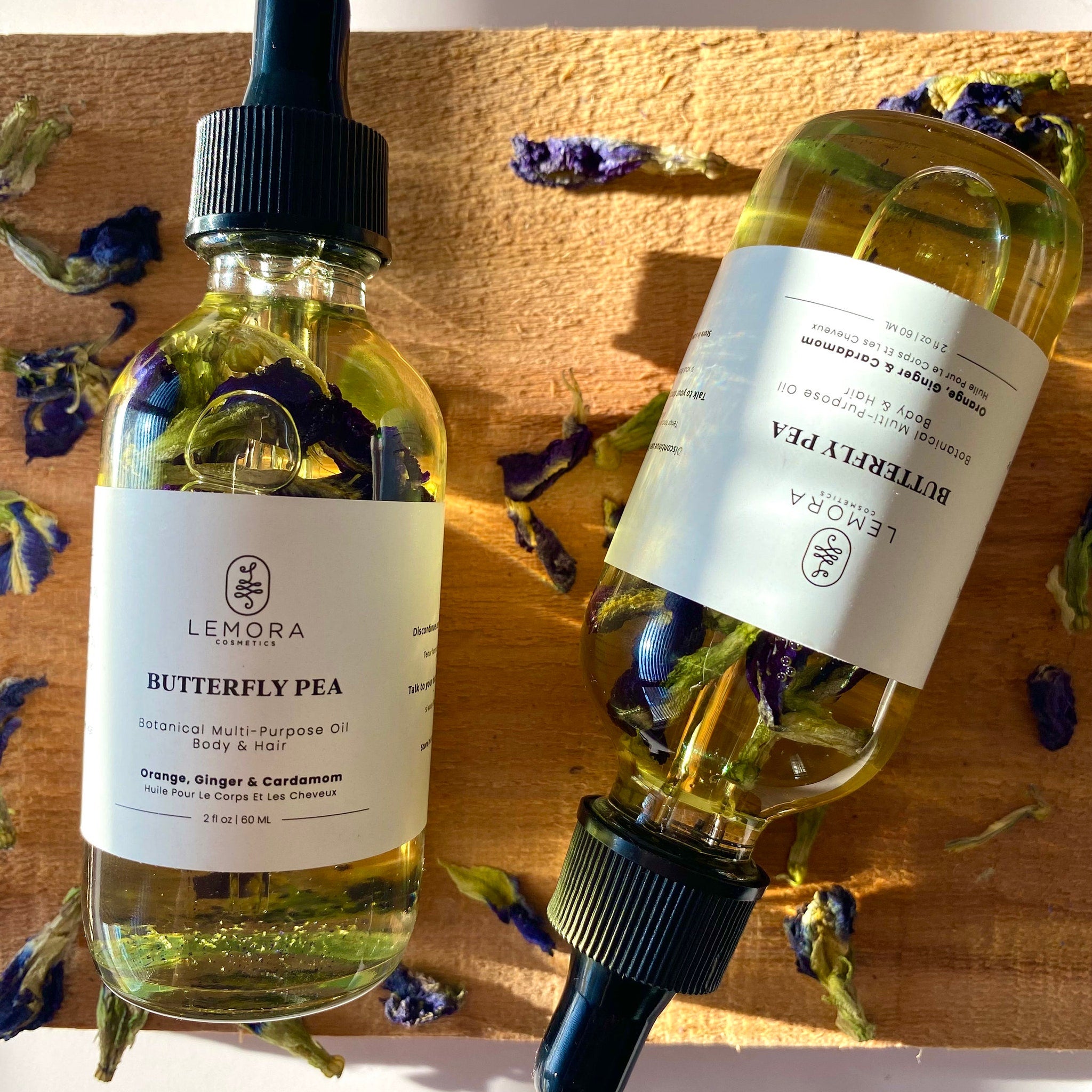 Butterfly pea oil bottles with black droppers, yellow liquid, and blue flowers on wood surface.