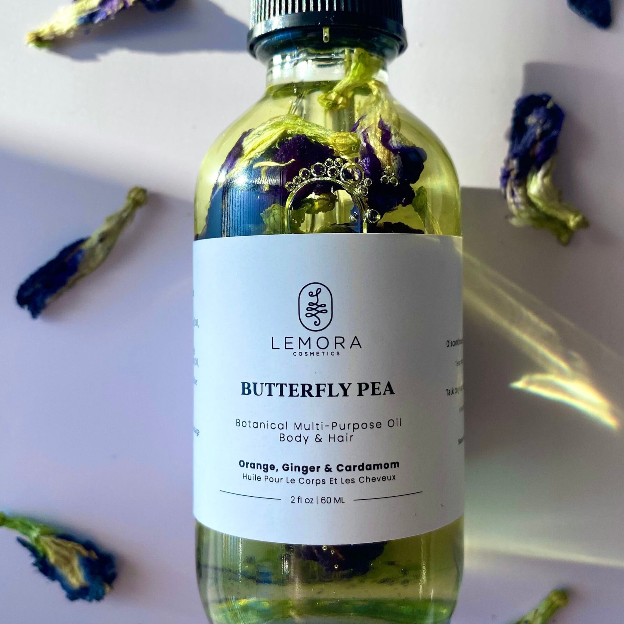 Butterfly pea oil bottle with clear liquid, blue flowers, and LEMORA label