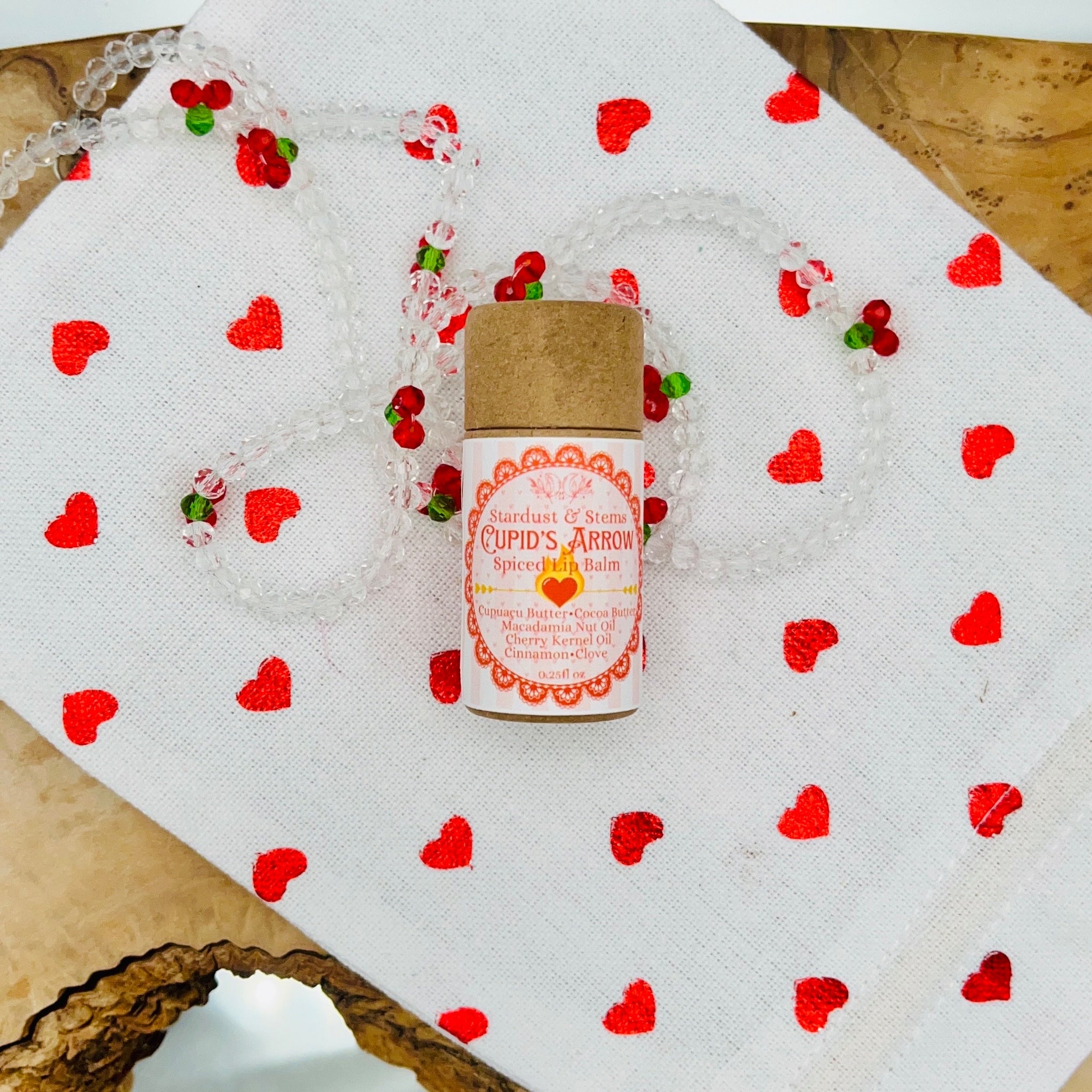 Lip balm tube with brown cap, pink and white label, and red heart pattern on white cloth
