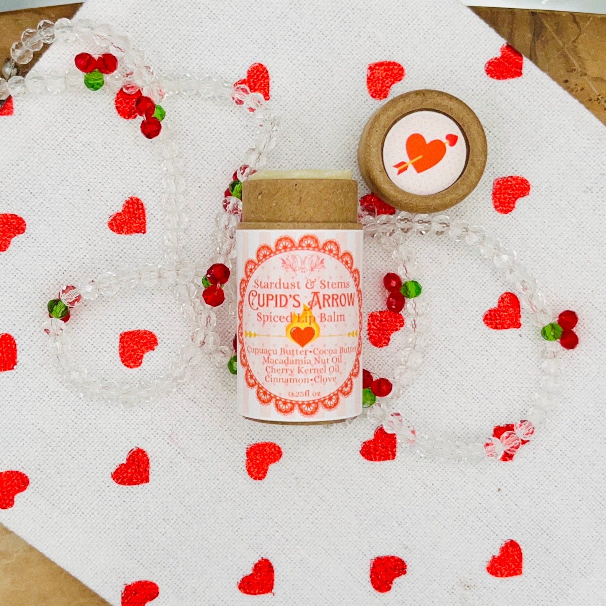 Lip balm tube with Stardust & Stems label, red heart pattern on white, clear beaded necklace