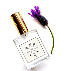 Perfume bottle with gold cap, clear glass, and "WR Luxe Oasis" label with a purple flower