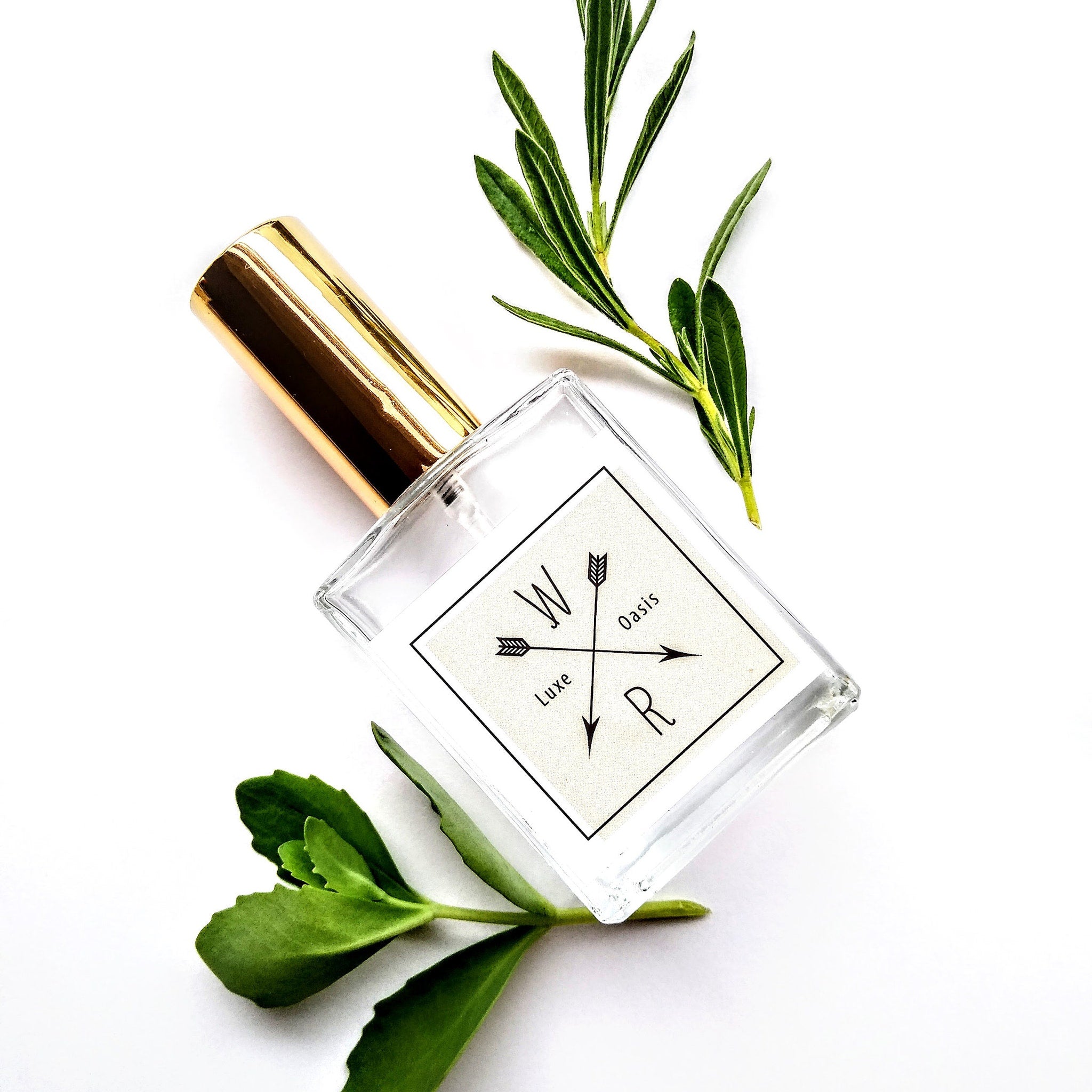 Perfume bottle with gold cap, clear glass, and "WXR Luxe Oasis" label with arrows on white background