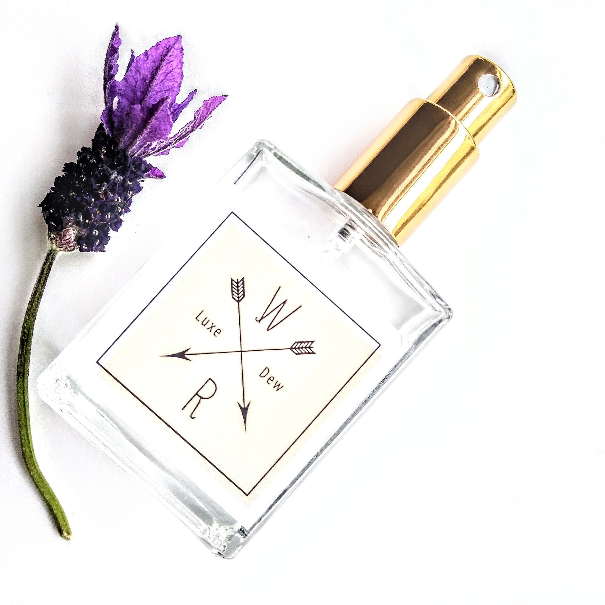 Perfume bottle with gold cap, clear glass, and "W Dew" label with purple flower accent