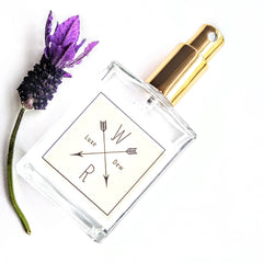Perfume bottle with gold cap, clear glass, and "W Dew" label with purple flower accent
