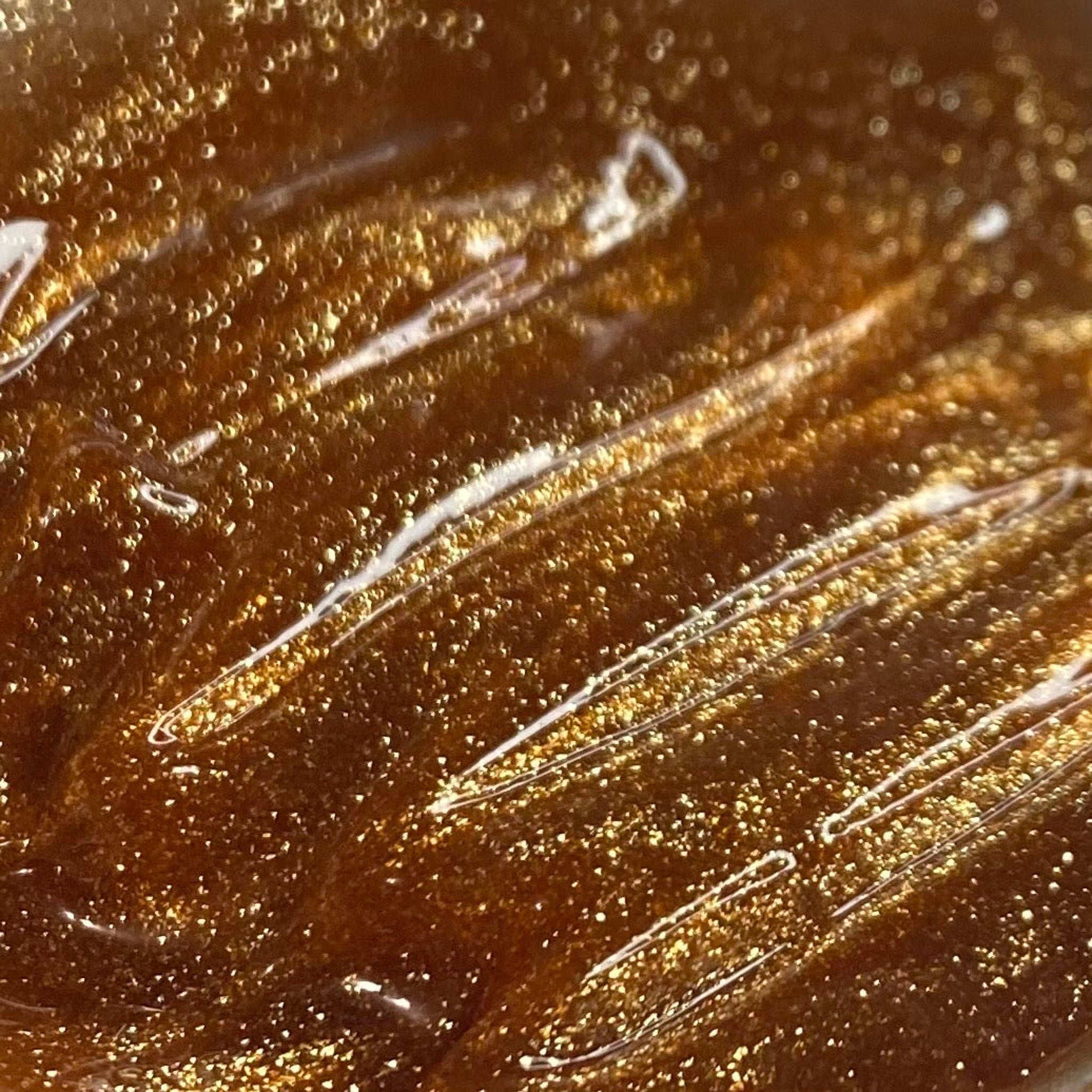 Glittery liquid with gold and brown tones, and white streaks across the surface