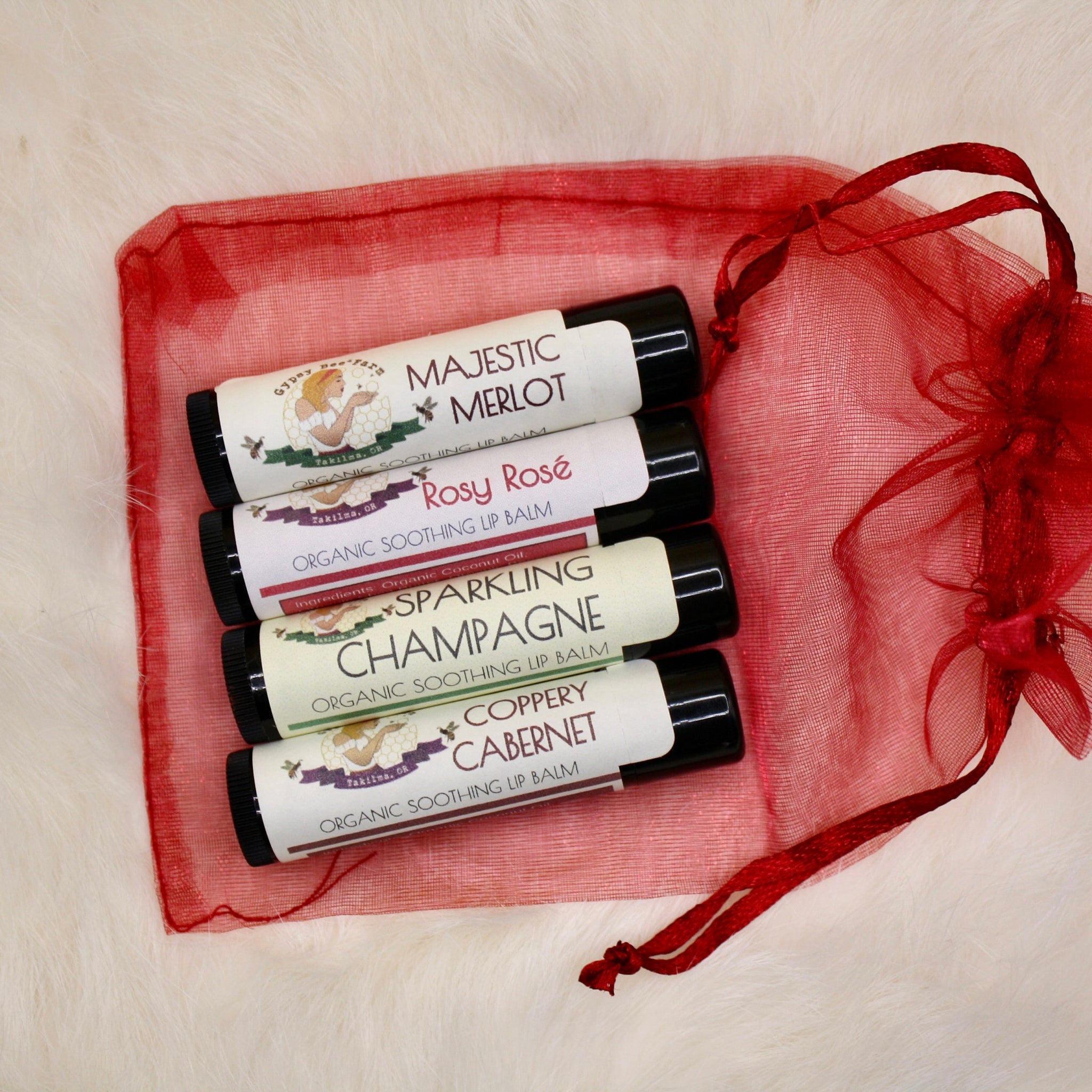 Lip balms in black tubes with white labels, in a red mesh bag on white fur background