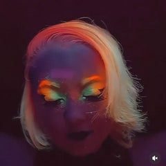 Eight vibrant neon matte eyeshadow pans in fluorescent shades arranged in a circular palette with UV glow effect