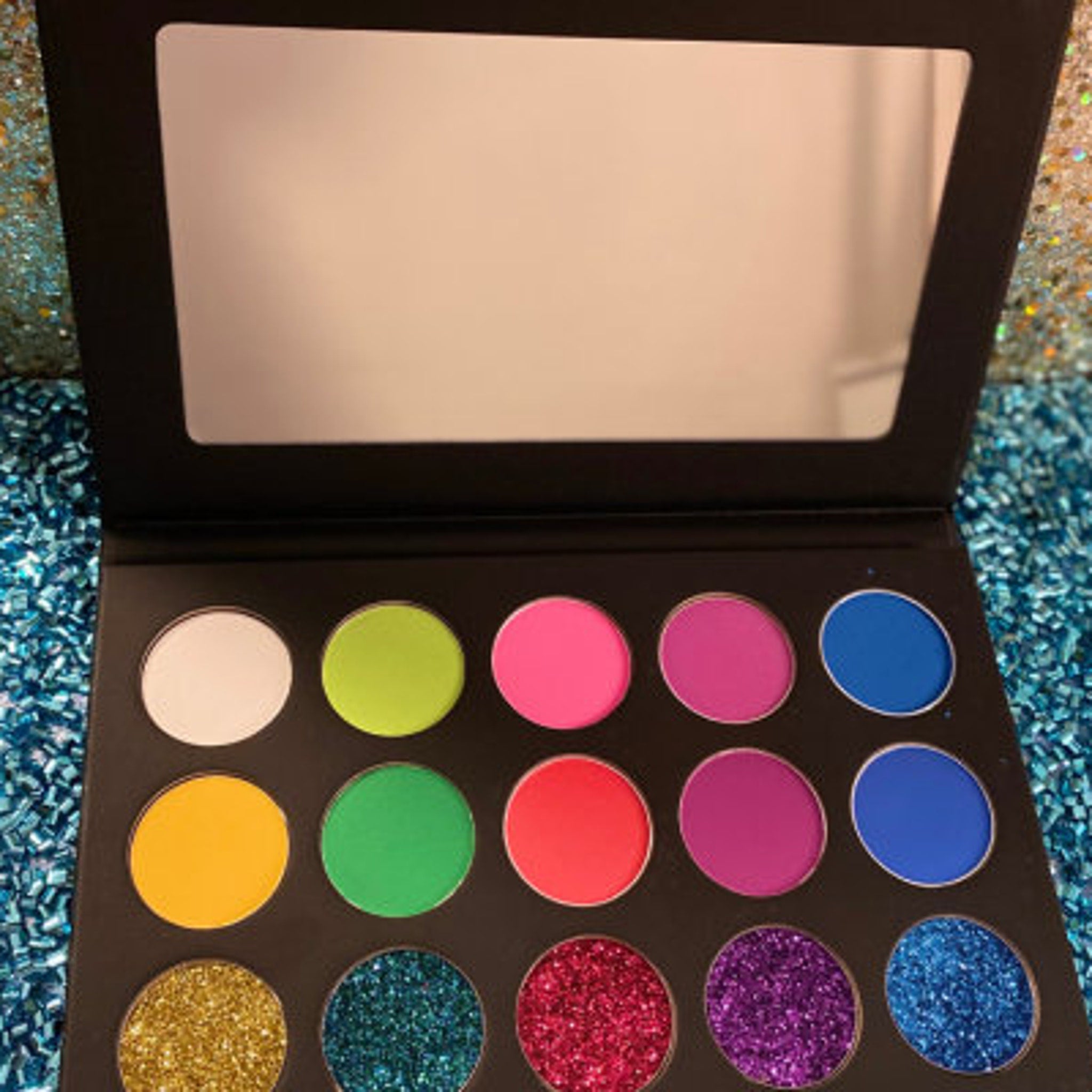 Vegan eye shadow palette with vibrant matte and glitter shades in a sleek black compact.