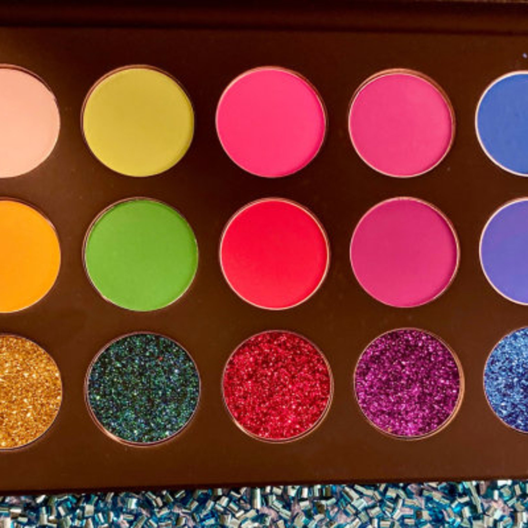 Side view of vegan cruelty-free eye shadow palette showcasing shimmering teal and silver glitter shades in compact case