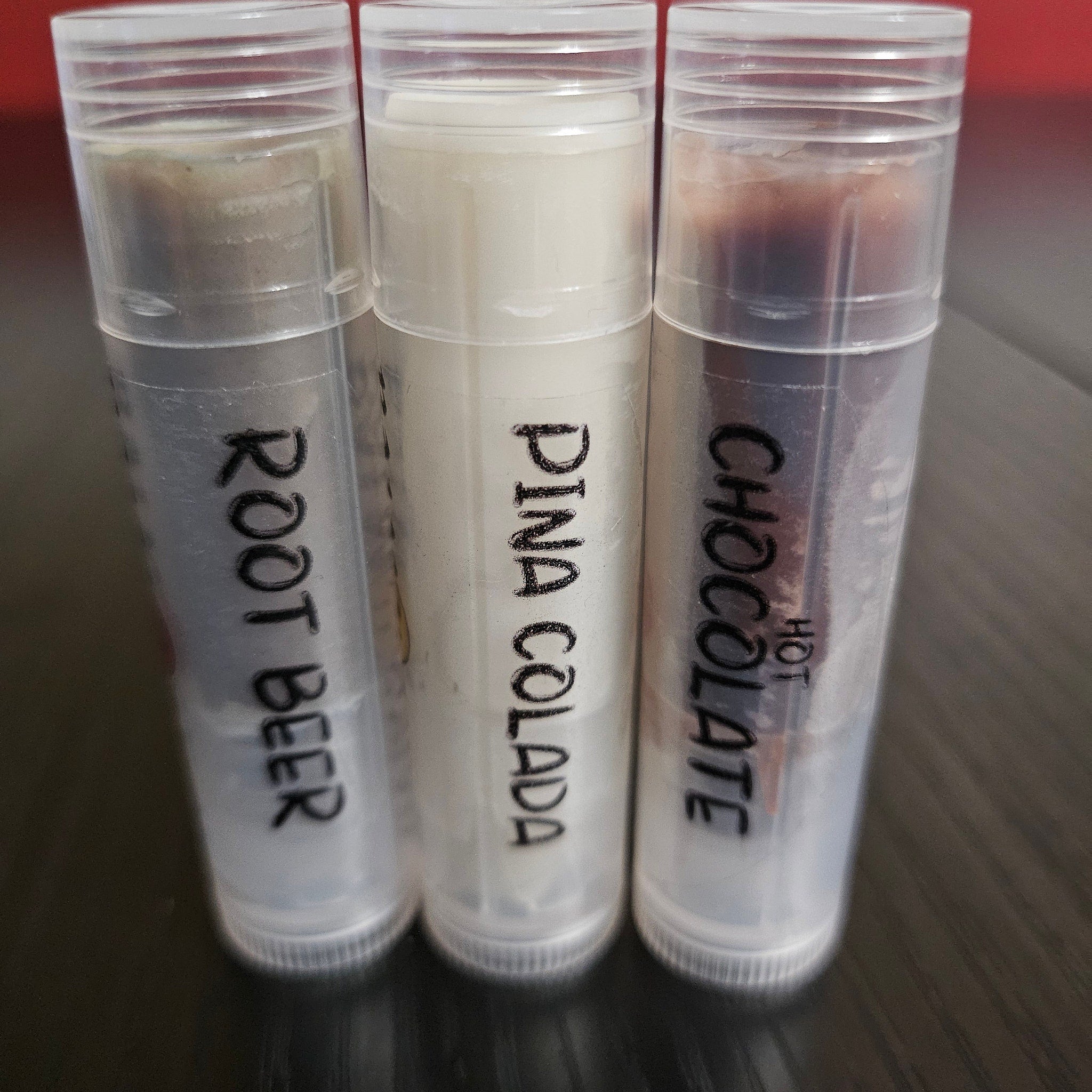 Lip balm tubes with root beer, pina colada, and chocolate labels in clear plastic containers