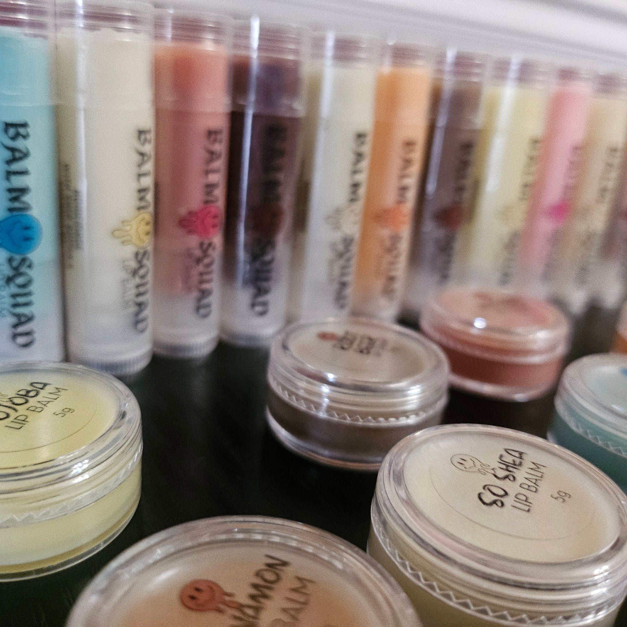 Lip balm tubes in various colors, clear plastic containers, and "BALM SQUAD" text visible