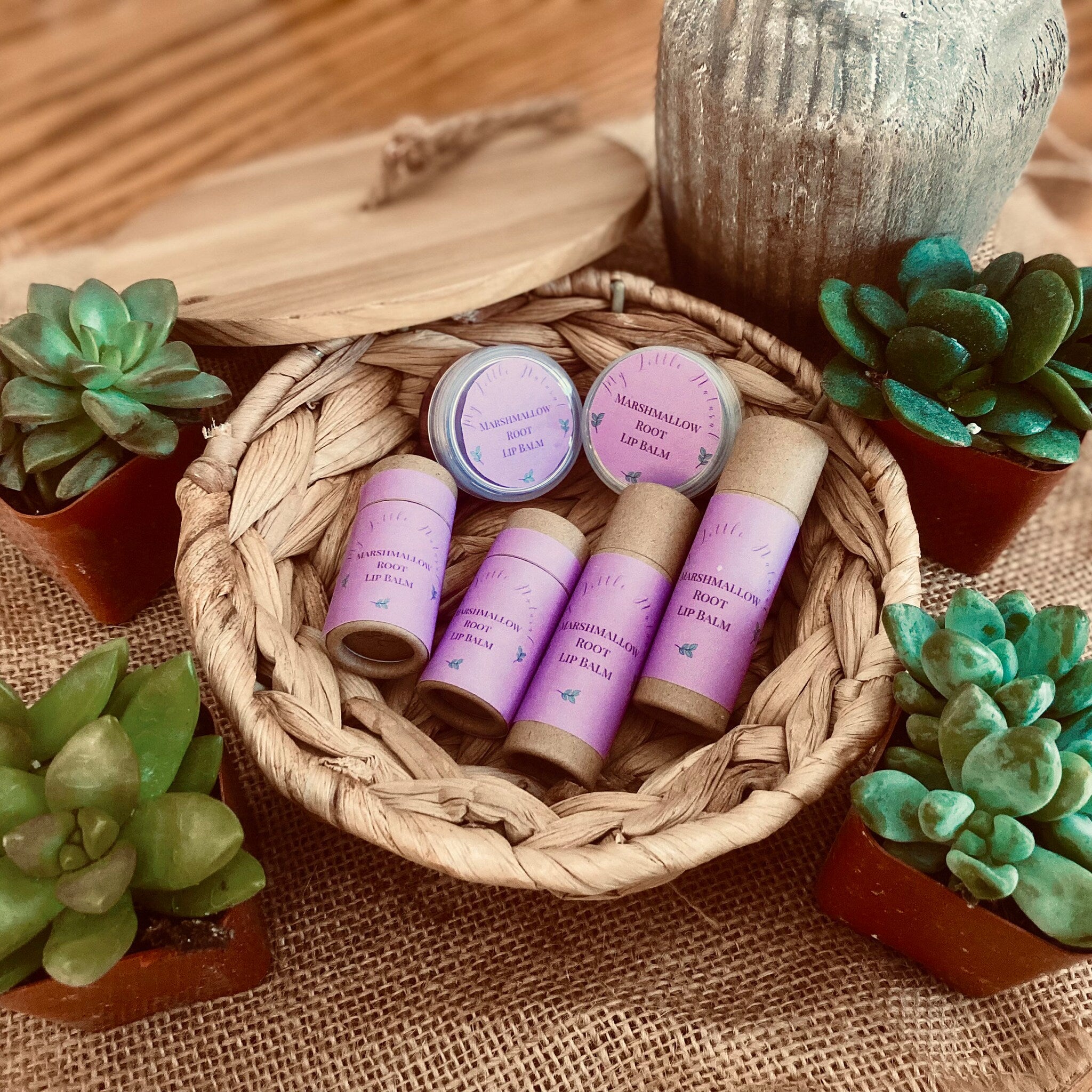 Lip balm tubes and jars in a woven basket with purple labels and green plants around