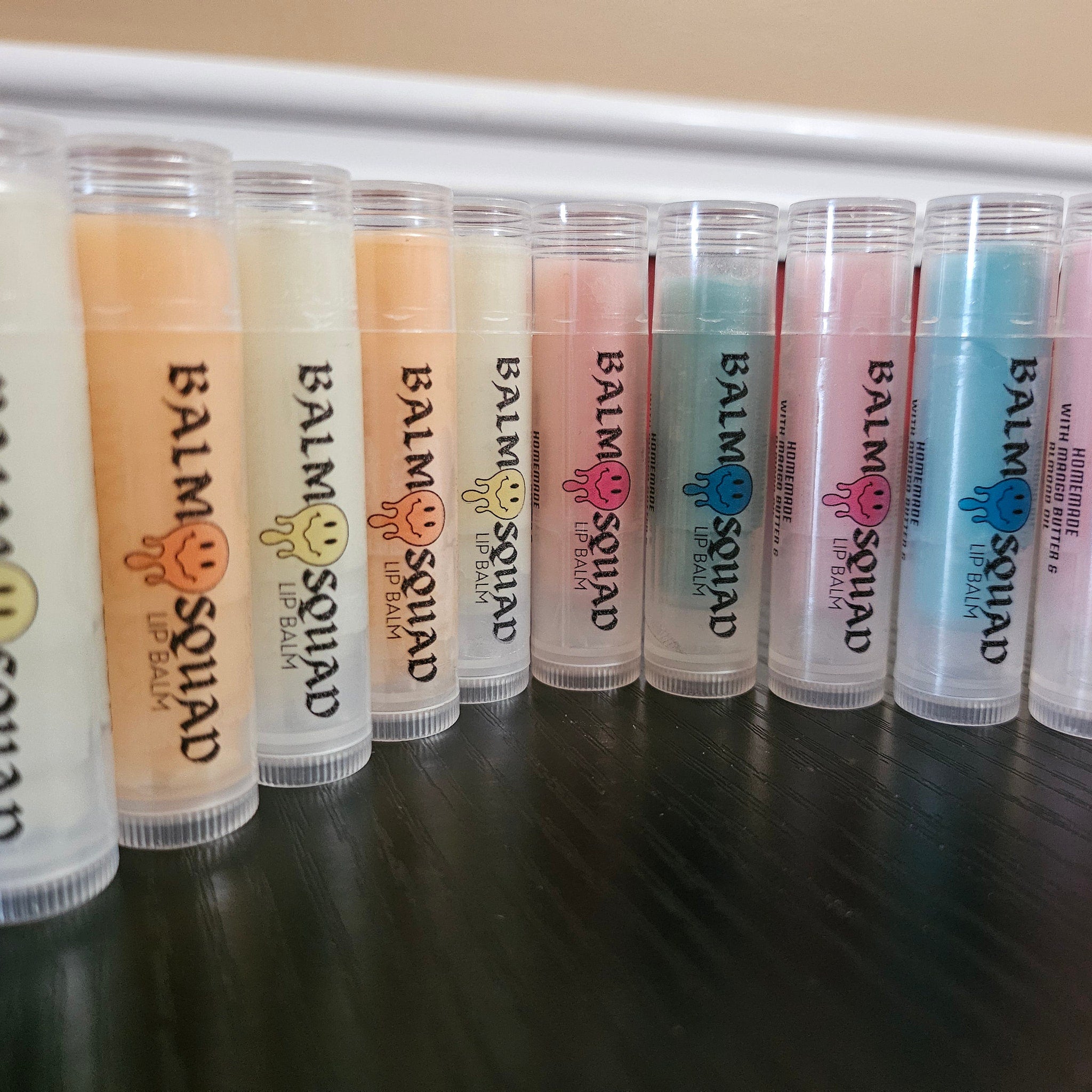 Lip balm tubes in various colors with Balm Squad logo and text, clear plastic containers
