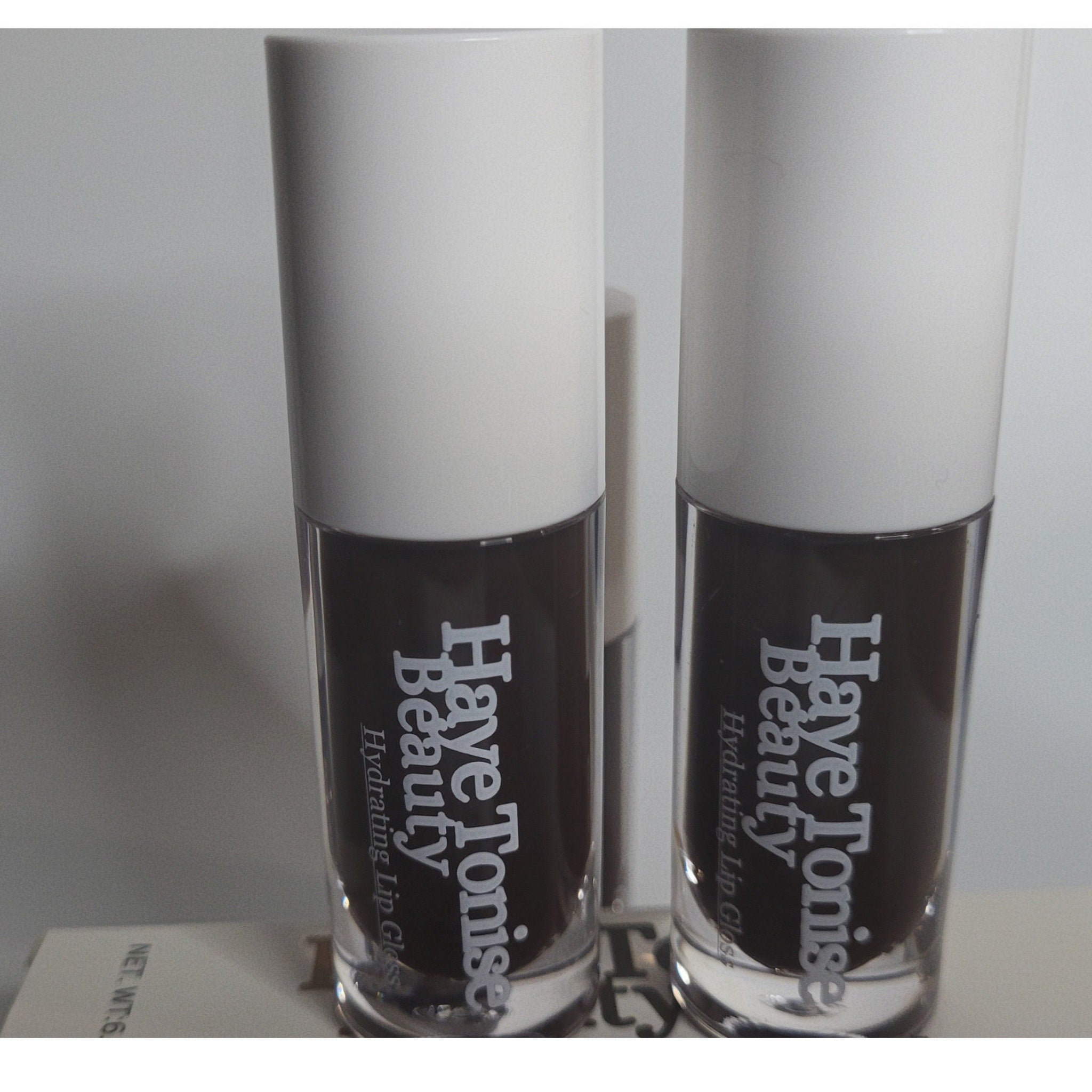 Lip gloss bottles with white caps, dark brown liquid, and Haye Tonise Beauty text visible