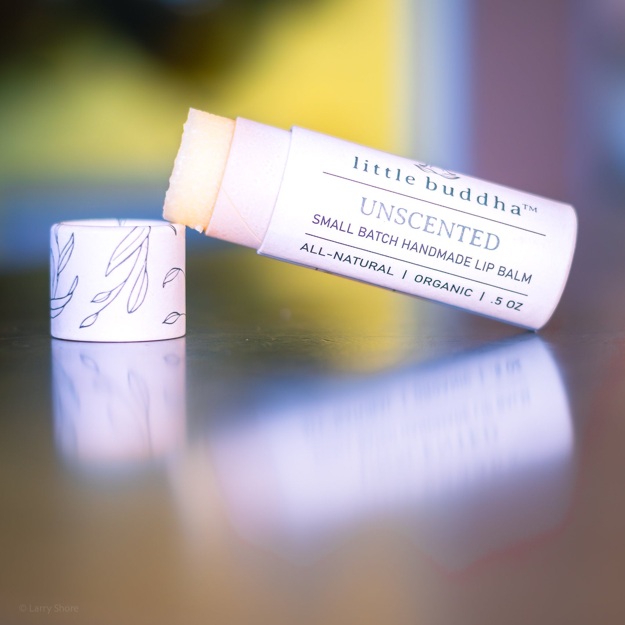 Lip balm tube with white and leaf pattern, light pink and beige balm, "little buddha" brand name visible