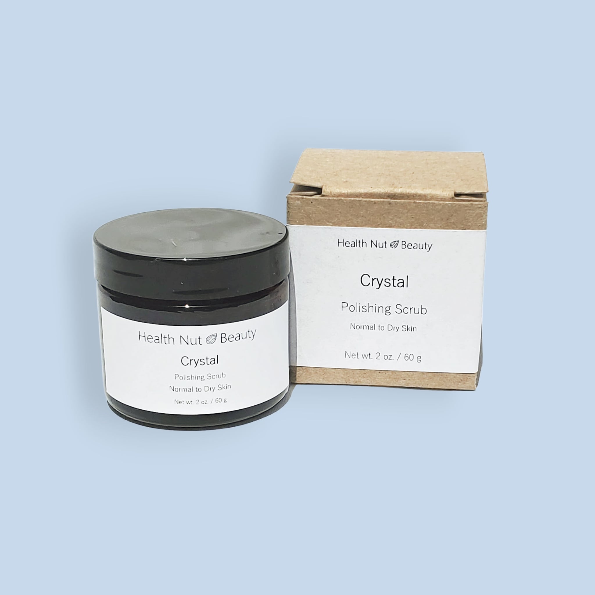 Facial scrub jar with black lid and white label, next to a brown box with Health Nut Beauty text