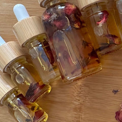Jojoba oil bottles with rose petals, clear glass, wooden lids, and amber liquid