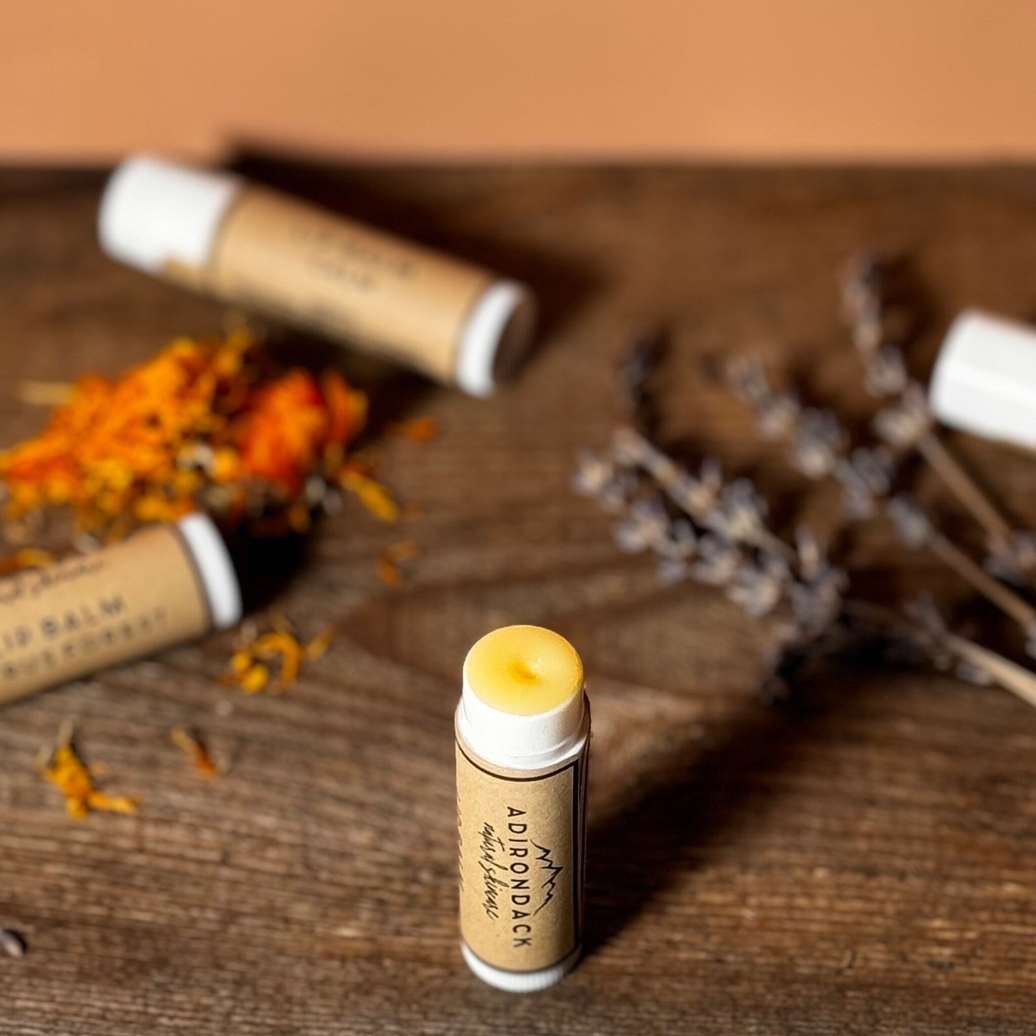 Lip balm tube with yellow balm, white cap, and Adirondack Natural Skincare label on wood surface