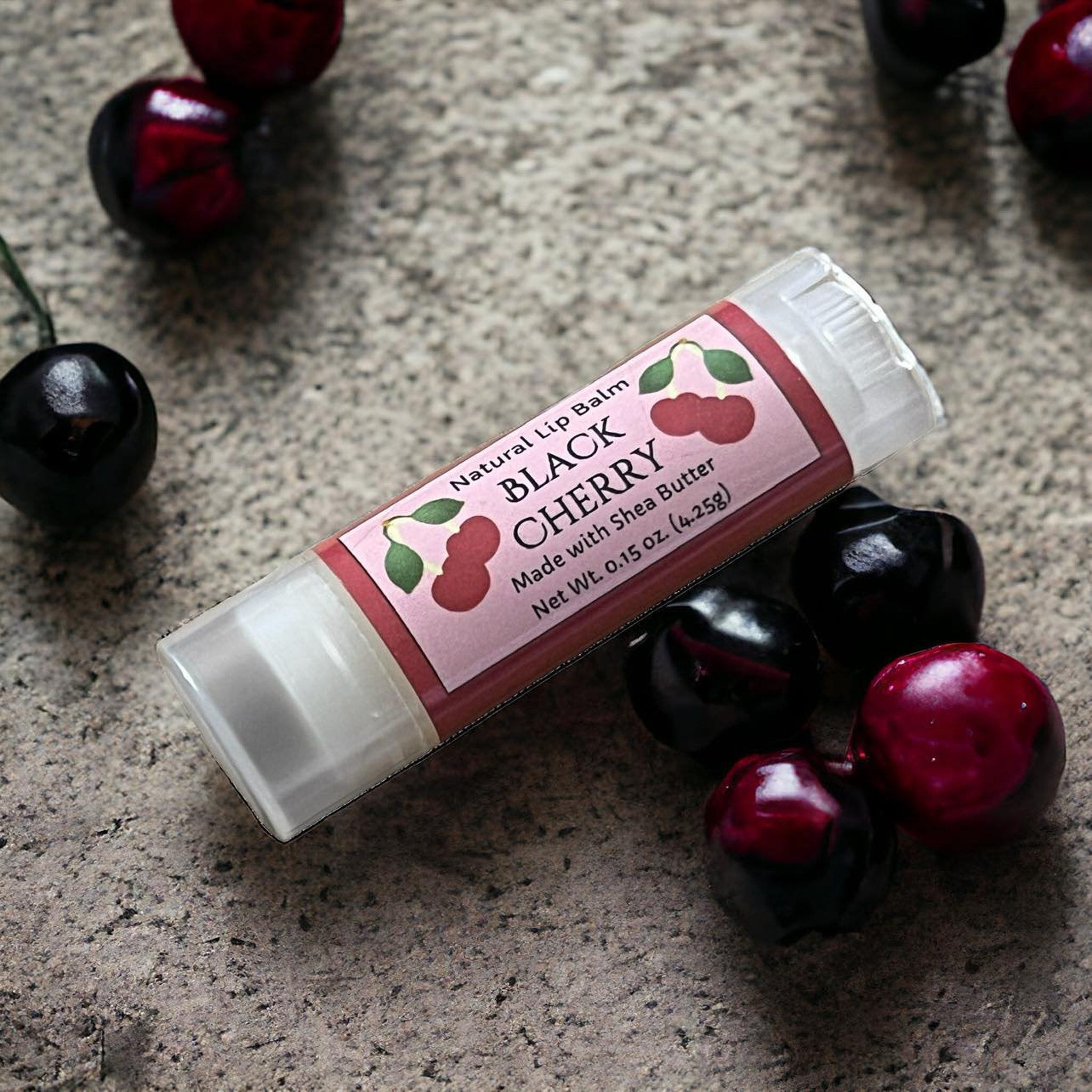 Lip balm tube with pink label, clear plastic, and black cherry fruit on stone surface