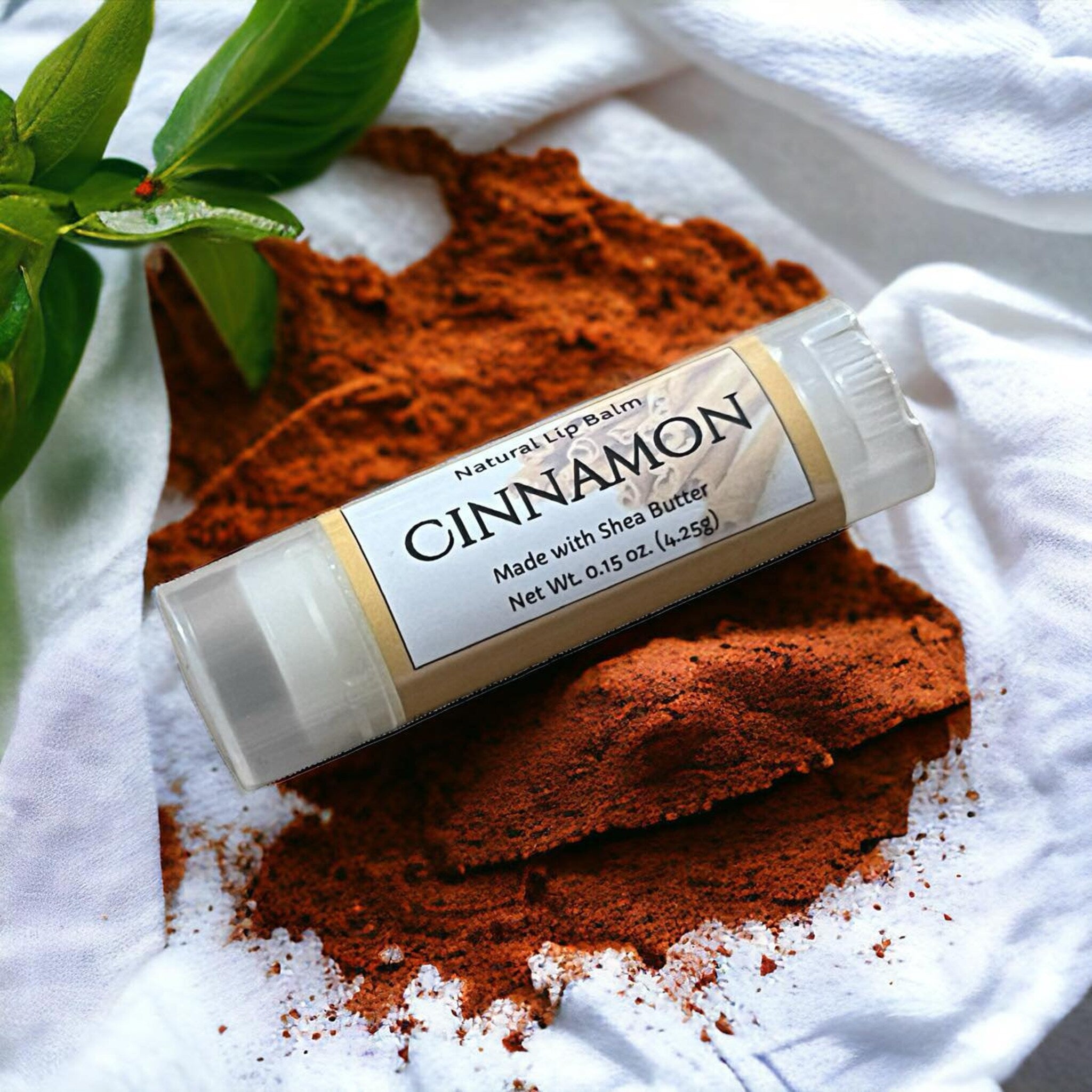 Lip balm tube with "CINNAMON" label, clear plastic, and white fabric background
