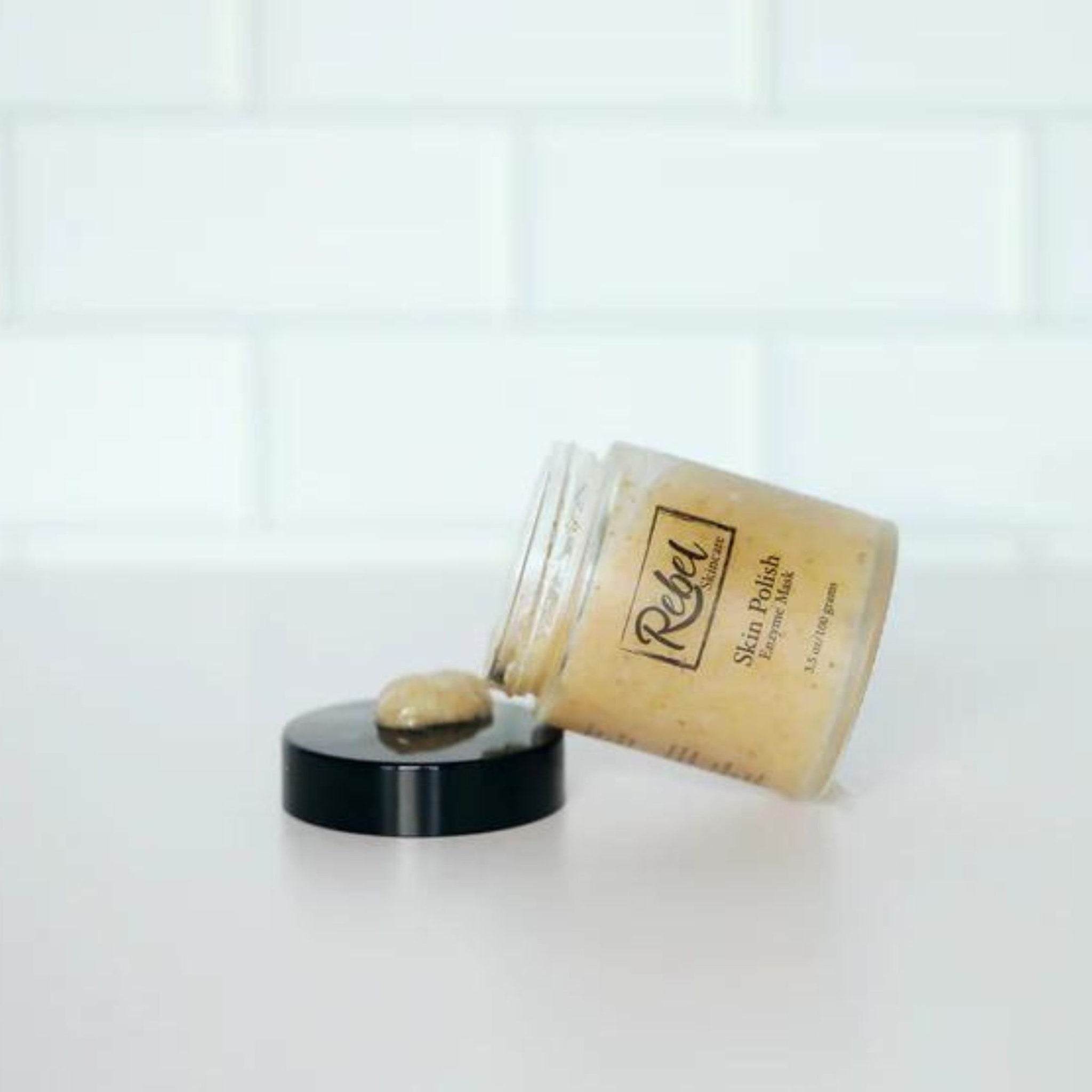 Skin polish jar with light brown contents, black lid, and Rebel Skincare label shown open