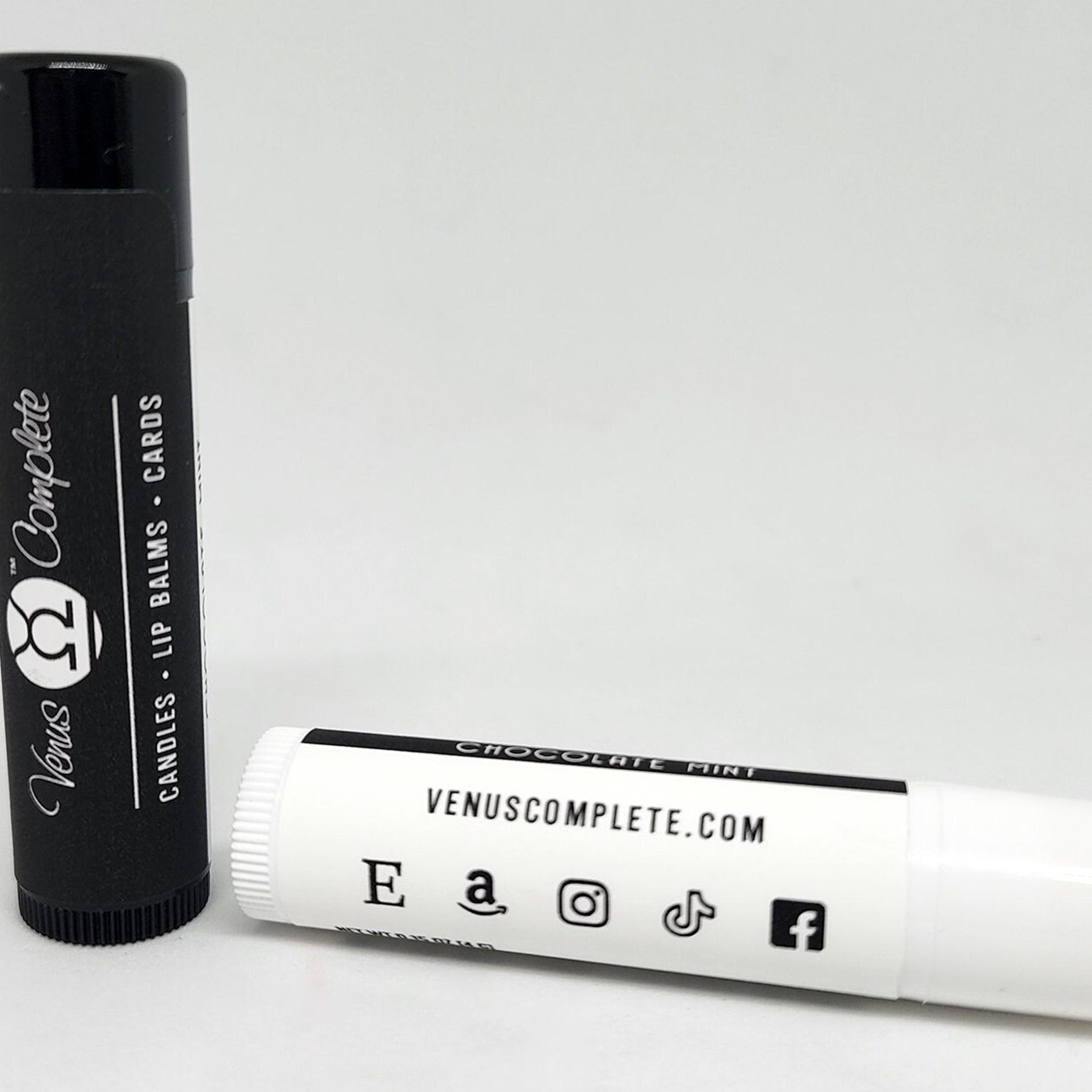 Lip balms, black and white cylindrical tubes with Venus Complete branding and social media icons