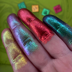 Close-up of fingers applying multichrome Rubrum eyeshadow with shimmering red-to-green shift on eyelid