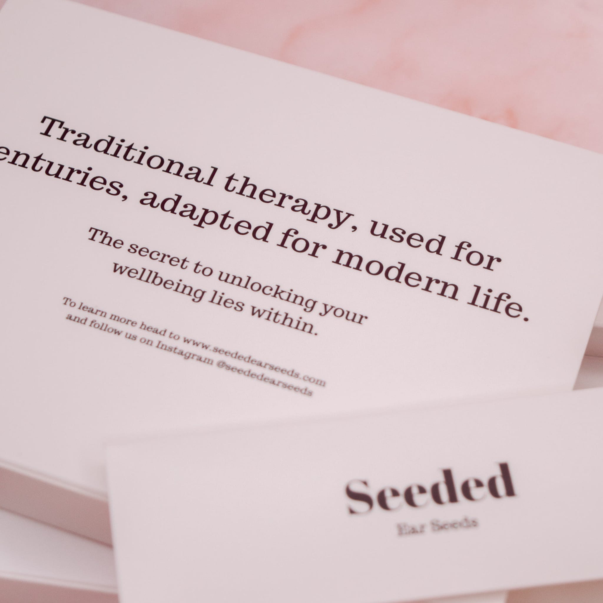 Seeded Ear Seeds branding on white paper with pink background, text about therapy and wellbeing