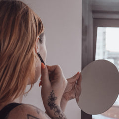 Woman holding mirror with red nails and floral tattoo, using tweezers