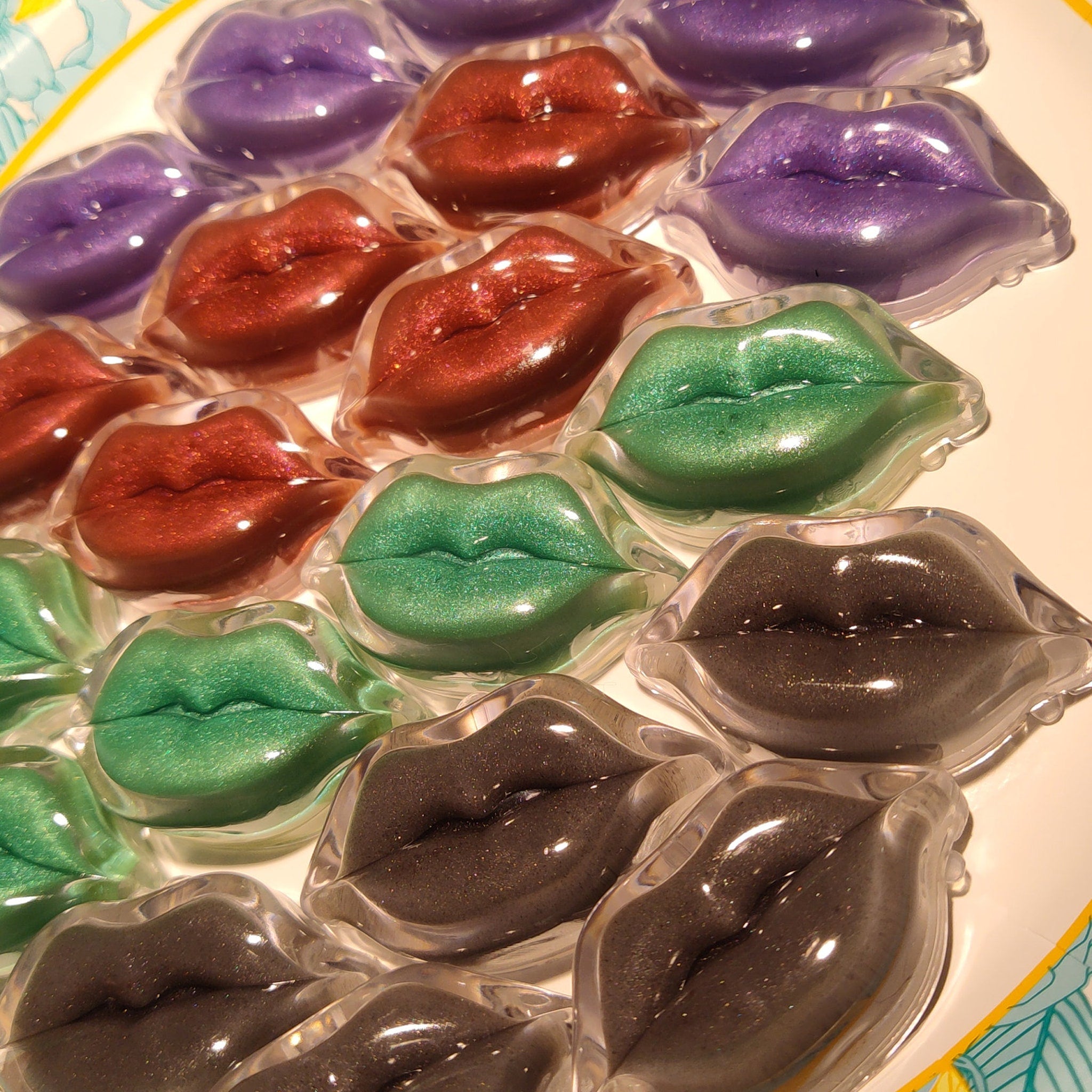 Lip-shaped cosmetic pods in various colors, including green, red, and purple, with glitter finish