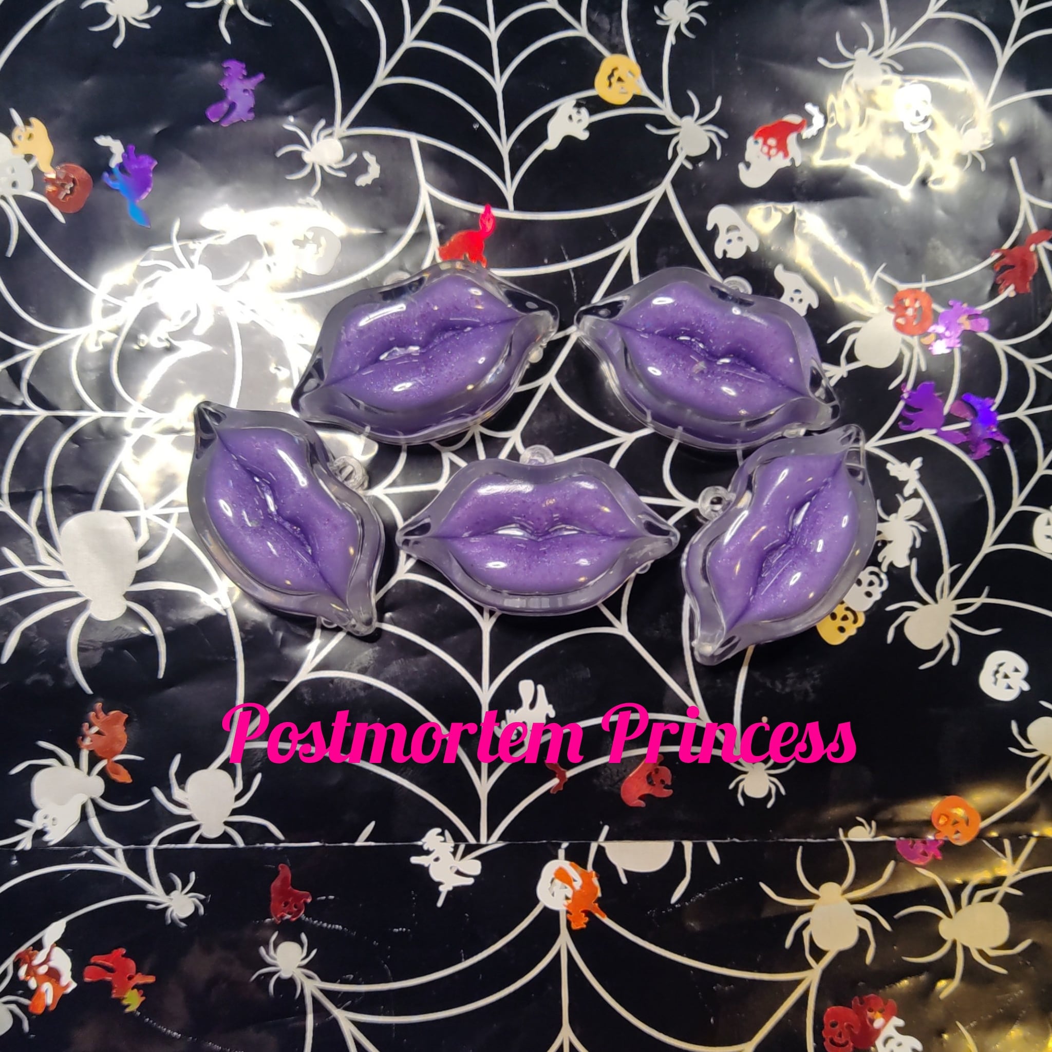 Purple lip shaped accessories with glitter, clear casing, and Halloween spiderweb background.
