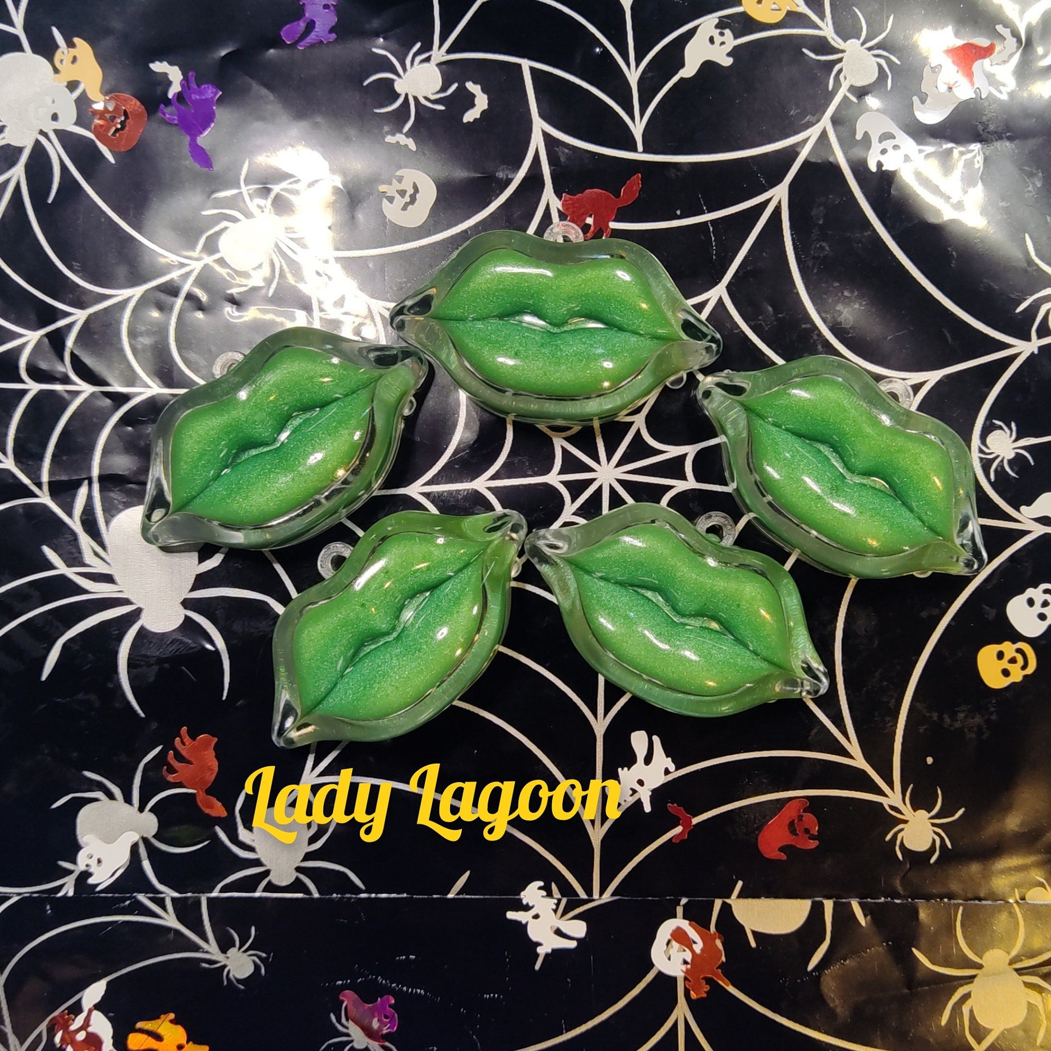Green lip-shaped ornaments with glitter, clear edges, and Lady Lagoon text on Halloween spiderweb background