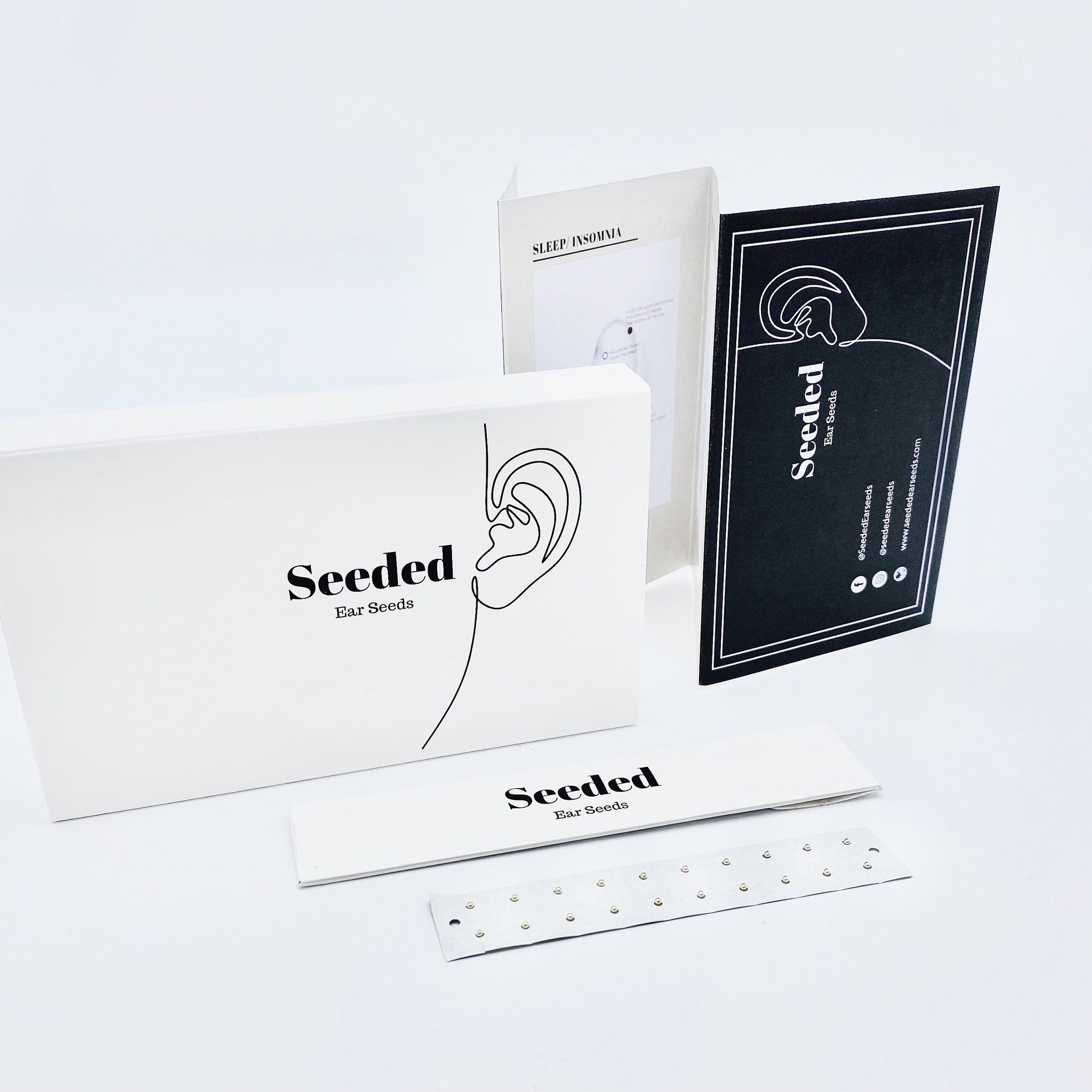 Ear seeds kit with white box, black text, and silver ear seeds on a strip.
