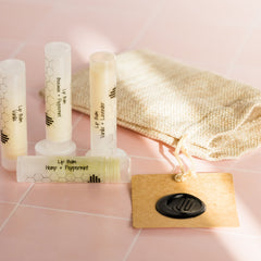 Lip balm tubes with white and honeycomb pattern, beige bag, and HandCraft Skincare tag on pink tile