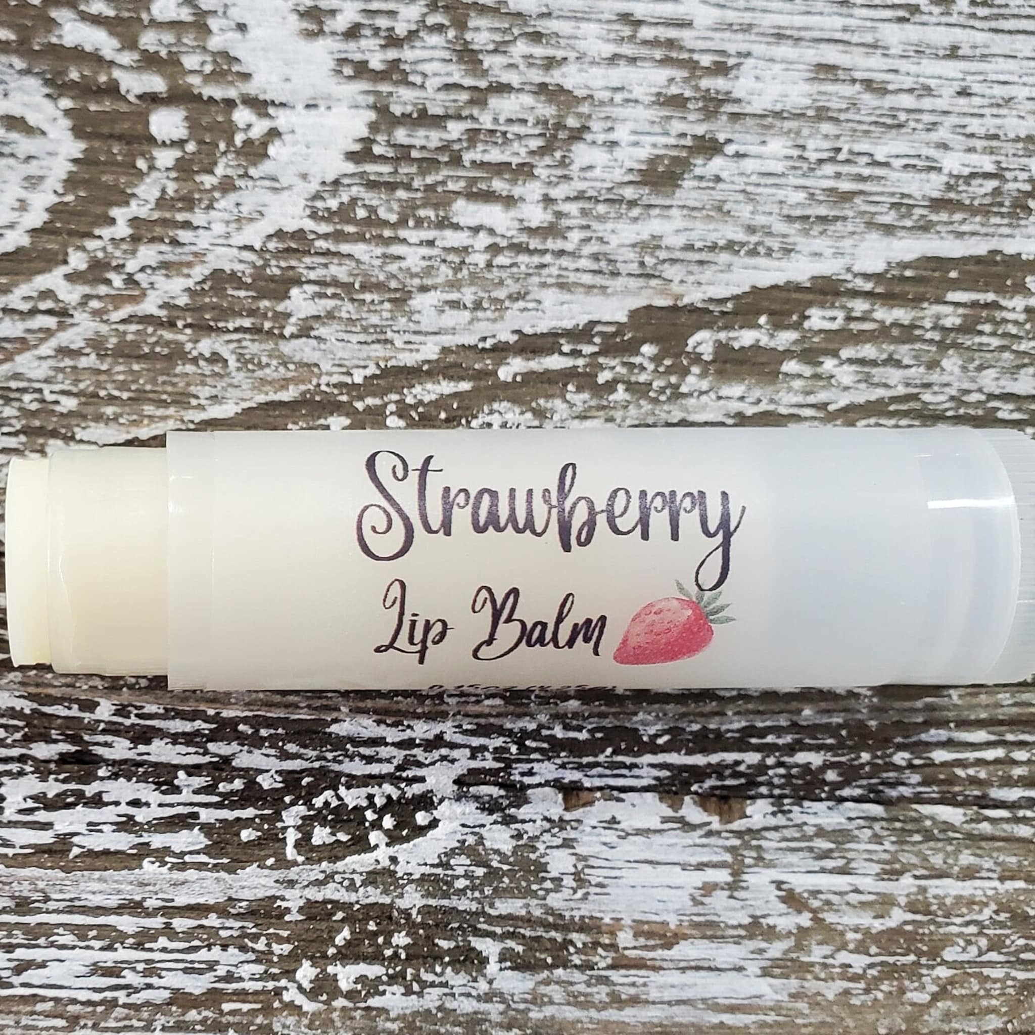 Lip balm tube with white label and "Strawberry Lip Balm" text, on wood background