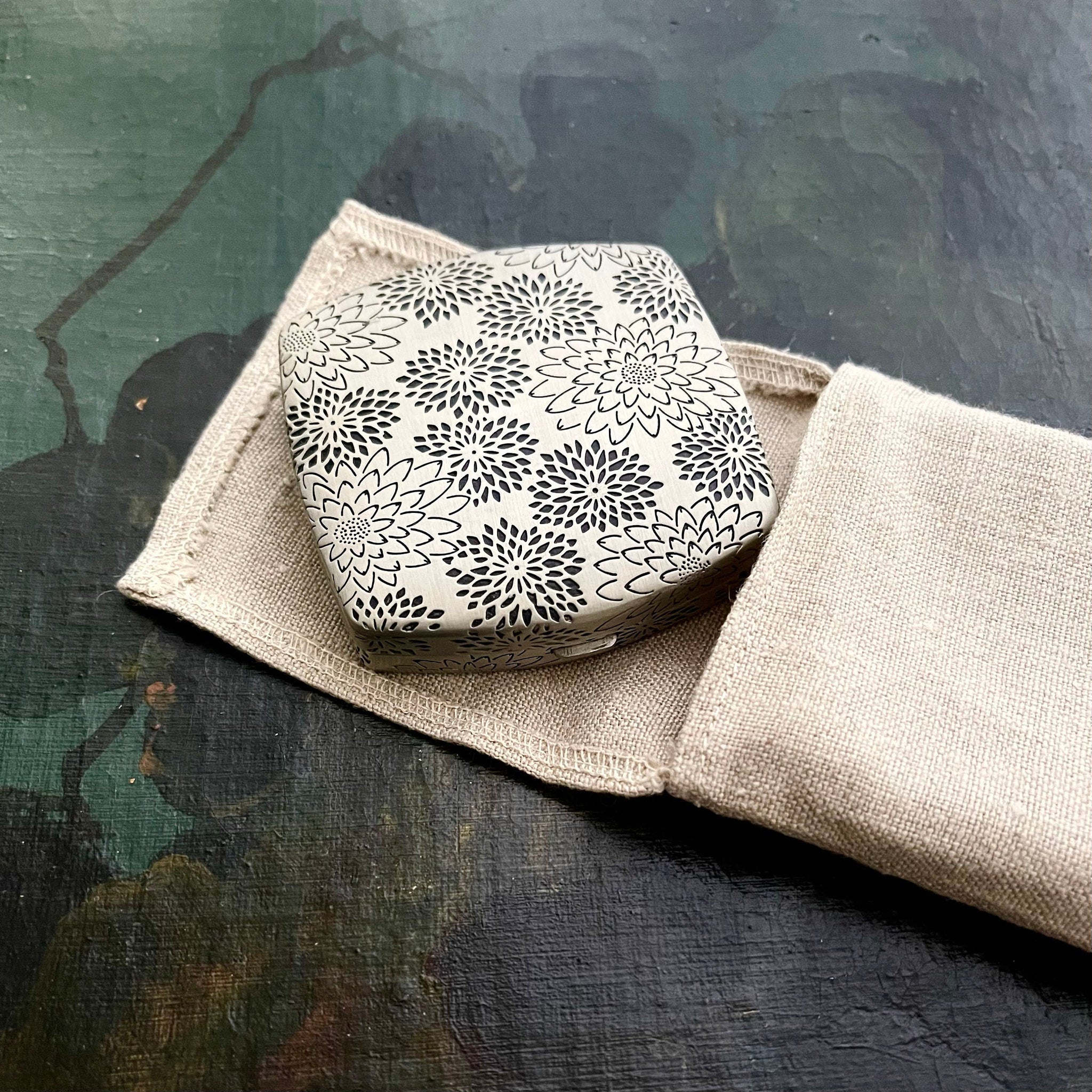 Floral pattern box in cream and black, resting in a beige linen pouch