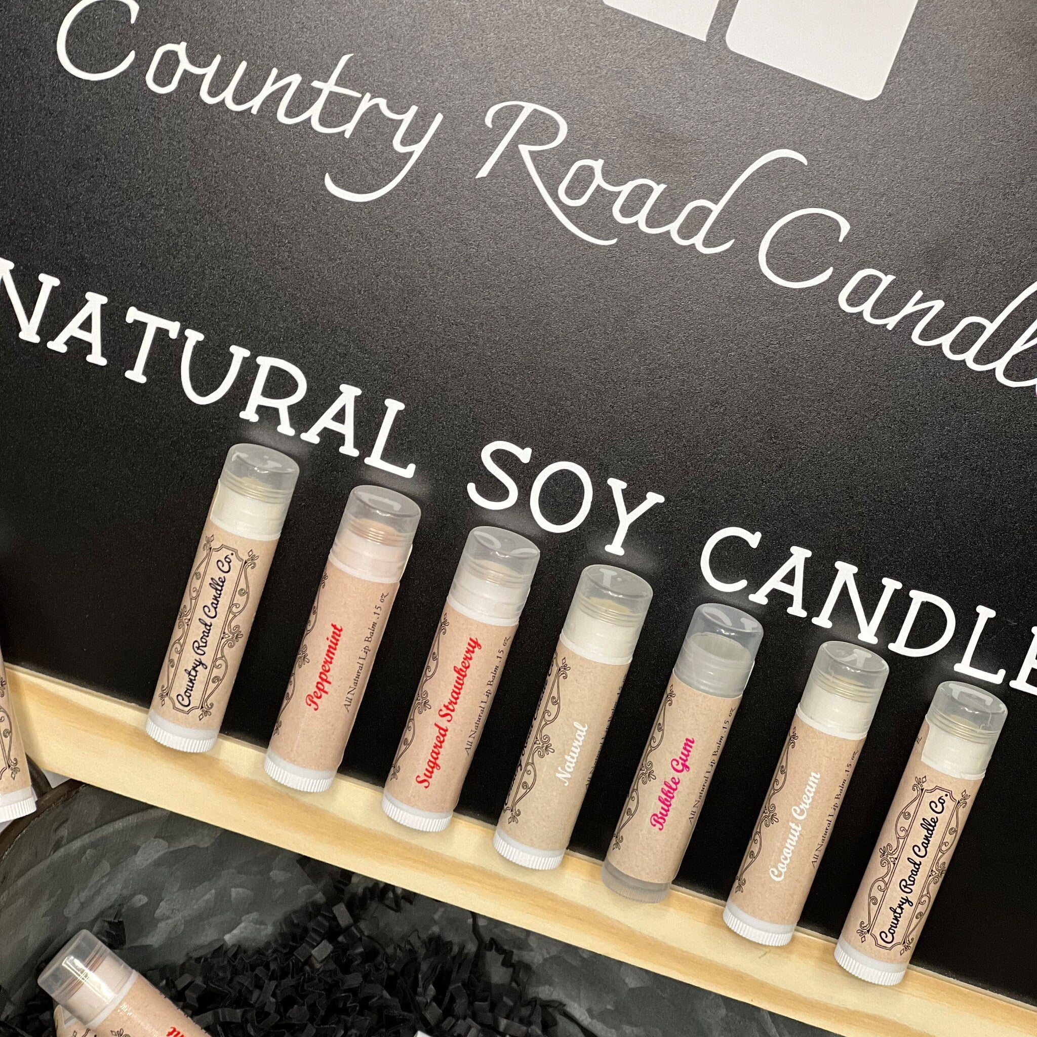 Lip balms with brown and white labels, Country Road Candle Co branding, and clear caps