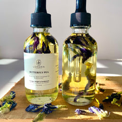 Butterfly pea oil bottles with clear glass, yellow liquid, and purple flowers on wood surface