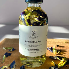 Hair oil bottle with purple flowers, clear liquid, and Lemora Cosmetics label on wood surface